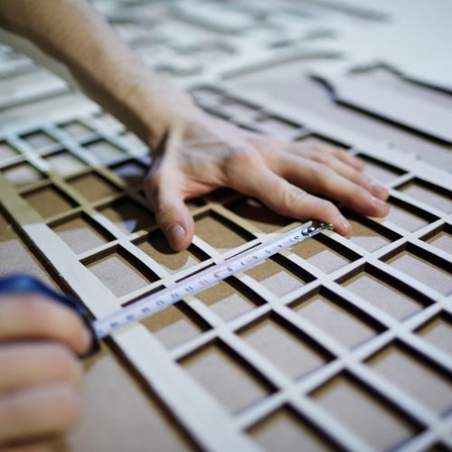Hands of craftsman measuring plywood sheet with cut cells