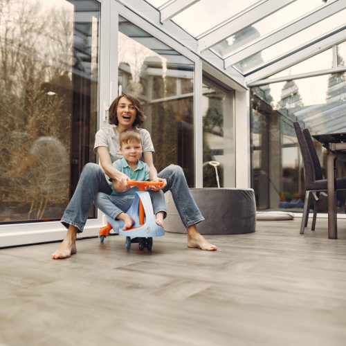 Beautiful woman with child. Woman in a gray t-shirt. Family go around the apartment on a toy car.